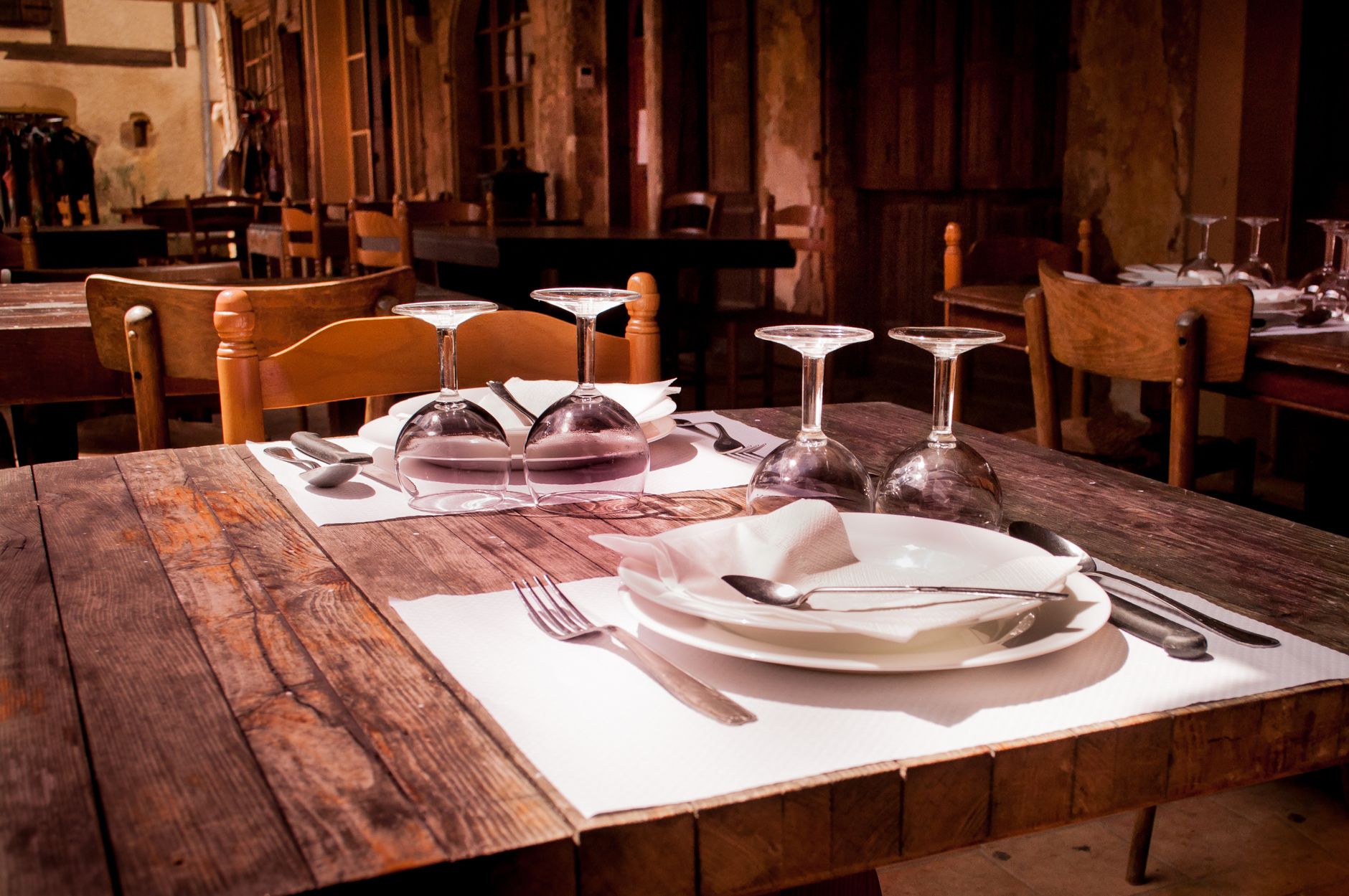 Wooden restaurant table set with white plates, napkins and upturned wine glasses